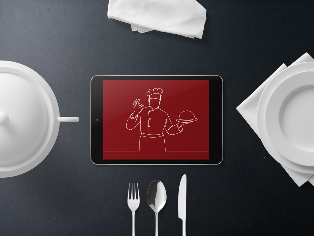 Draufsicht auf einen dunklen Tisch mit einem Tablet, das eine rote Fläche mit einer weißen Strichzeichnung eines Kochs zeigt, umgeben von weißem Geschirr, Besteck und Servietten.