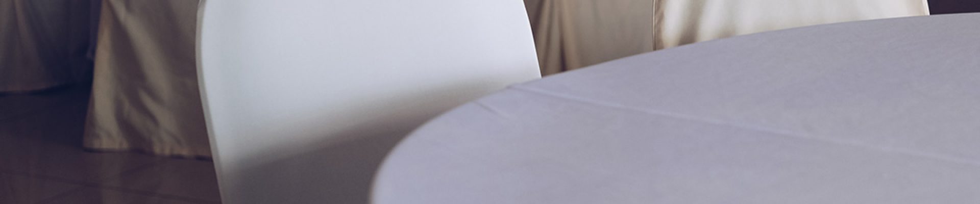 Leerer Bankettsaal mit mehreren runden, weiß gedeckten Tischen und Stühlen, die in cremefarbenen Hussen bezogen sind.