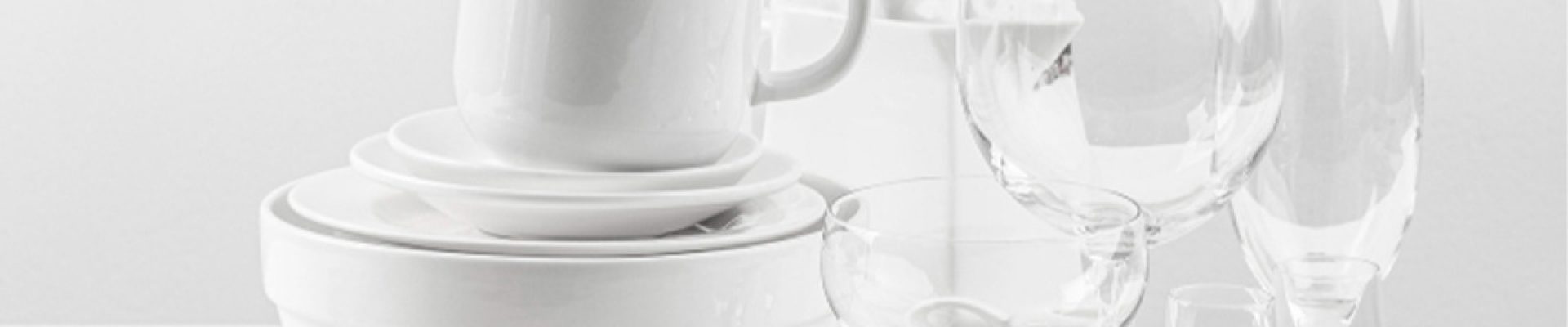 Gestapelte weiße Teller, Schüsseln und ineinander gesteckte Tassen links, daneben mehrere klare Weingläser und Sektgläser auf einem weißen, minimalistischen Hintergrund.